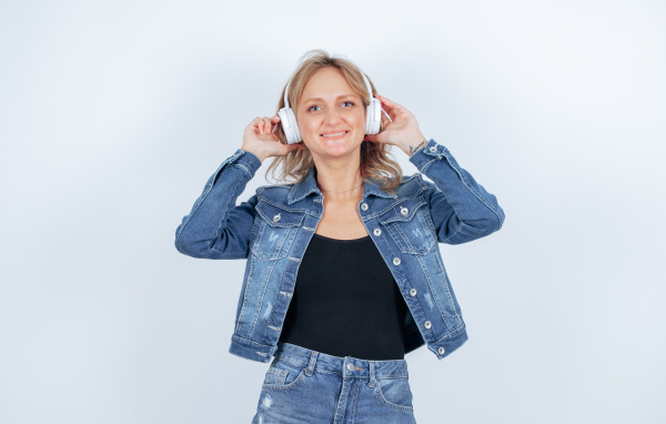 Девушка в джинсовом костюме с наушниками на голове на фоне стены