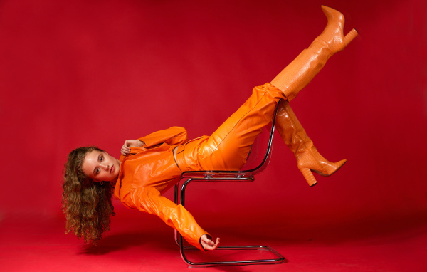 Девушка в кожаном костюме лежит на кресле на красном фоне