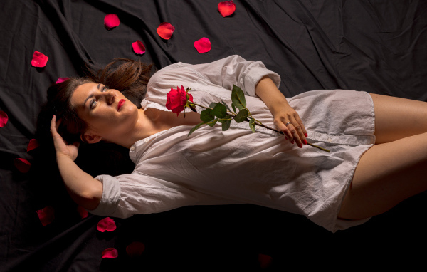 Девушка в белой рубашке с розой в руках лежит на постели