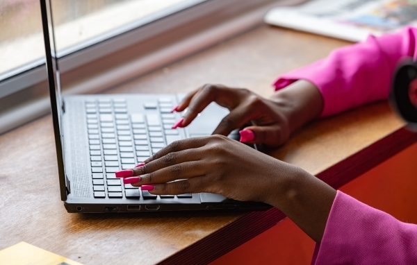 Девушка с розовым маникюром сидит за ноутбуком