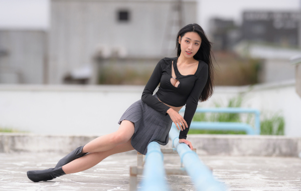 Девушка азиатка в черном наряде сидит на трубе