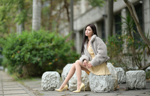 Азиатка в шубе сидит на квадратном камне