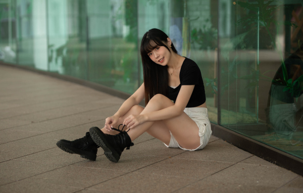 Азиатка в шортах сидит у стеклянной стены