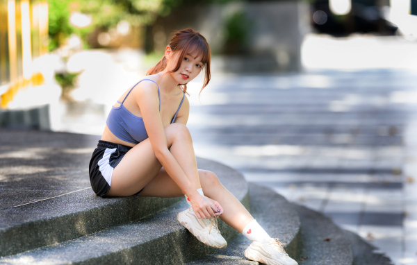Азиатка в шортах сидит на ступеньках