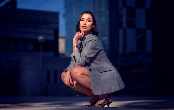 Красивая брюнетка в сером пиджаке сидит на корточках