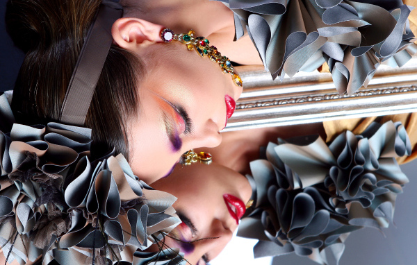 Красивая девушка с ярким макияжем отражается в зеркале