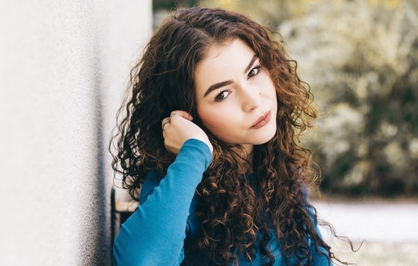 Кареглазая девушка с кудрявыми волосами стоит у стены