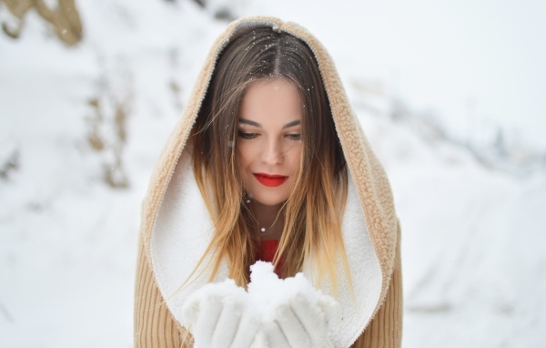 Милая девушка в капюшоне держит снег в ладонях
