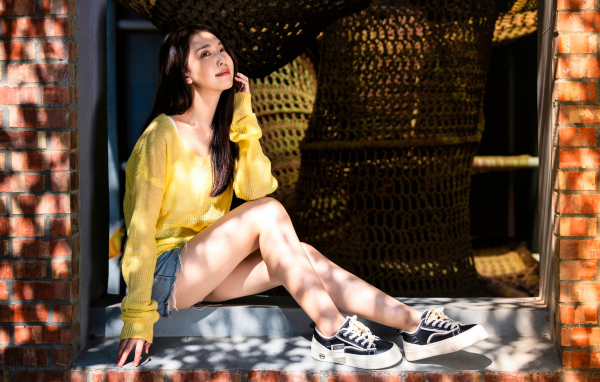 Мечтательная молодая девушка азиатка сидит на окне