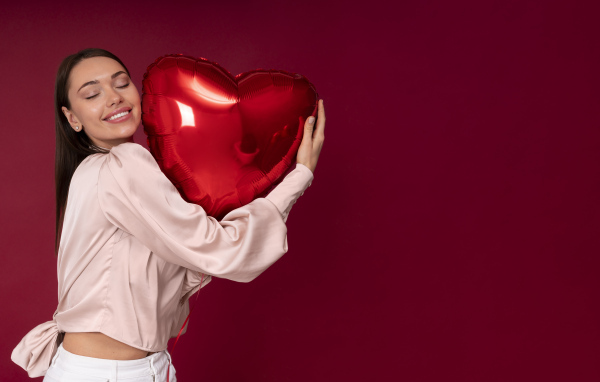 Девушка держит шарик в форме сердца на красном фоне