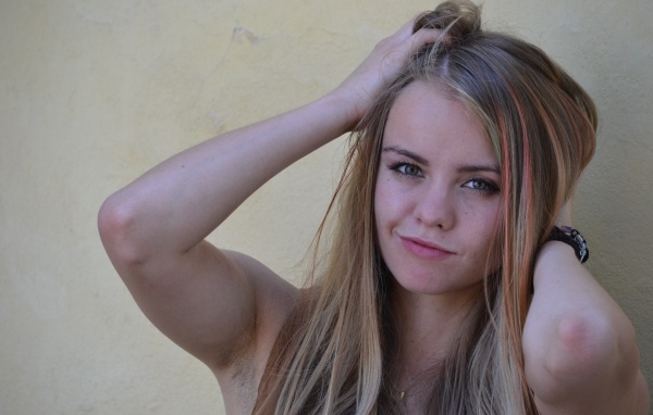 Девушка с руками в волосах у стены