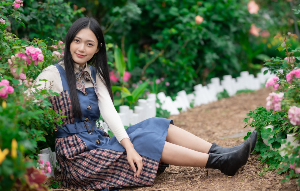 Настоящая молодая азиатка сидит на земле у клумбы