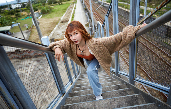 Рыжеволосая азиатка в кофте стоит на ступеньках