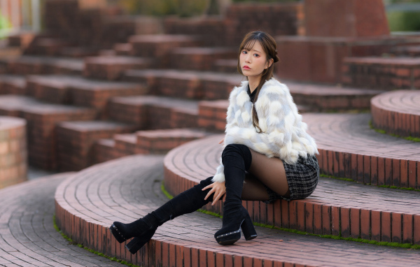 Грустная азиатка в шубе сидит на ступеньках
