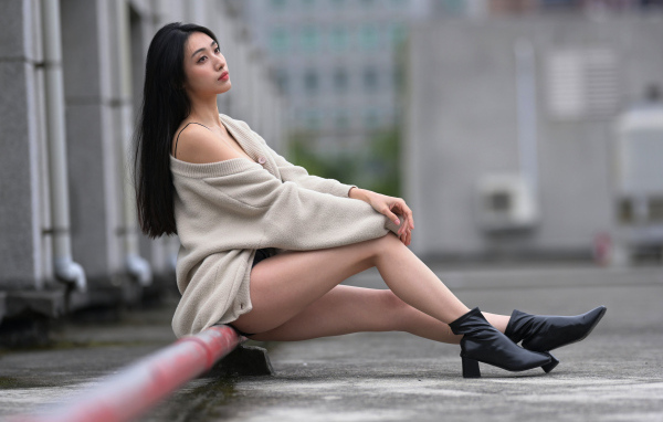 Грустная азиатка в теплой кофте сидит на трубе