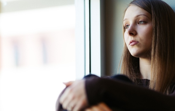 Грустная девушка сидит у окна