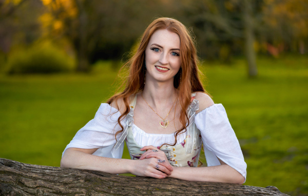 Улыбающаяся рыжеволосая девушка стоит у дерева