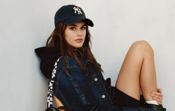 Красивая модель Кайя Гербер в кепке сидит у стены