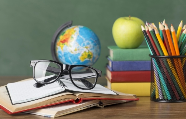Книги, очки и карандаши с глобусом на столе у доски