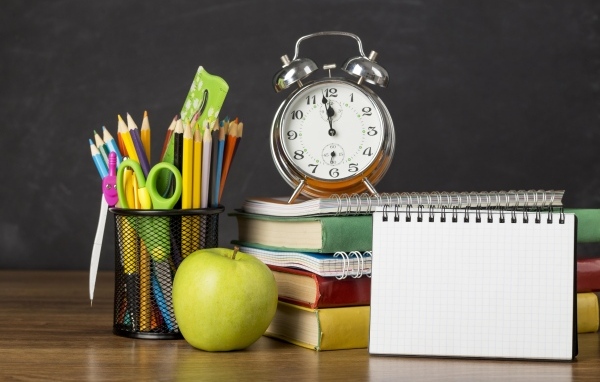 Канцелярские предметы на столе с будильником и книгами 