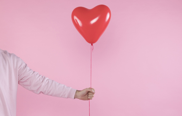 Шарик в форме сердца в руке на розовом фоне
