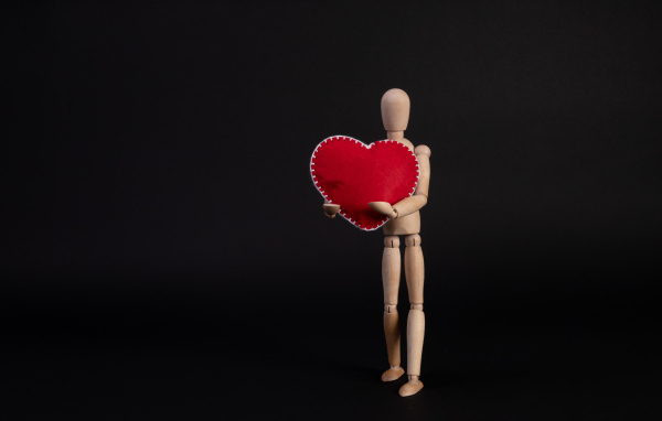 Марионетка держит красное сердце на черном фоне