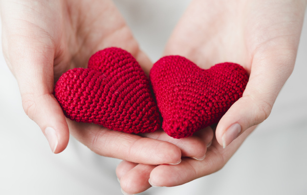 Два красных вязаных сердечка в руках девушки