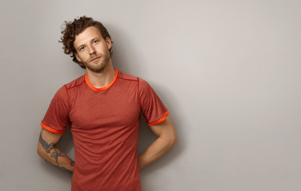 Мужчина в футболке стоит у серой стены