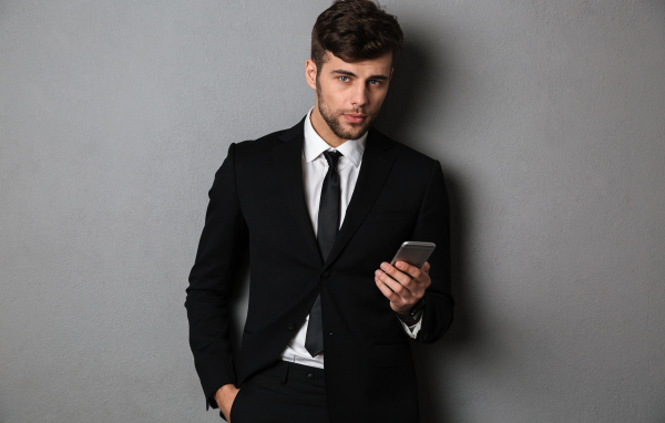 Деловой мужчина в костюме стоит у стены с телефоном