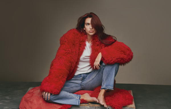 Певица Дуа Липа в красной шубе сидит на полу