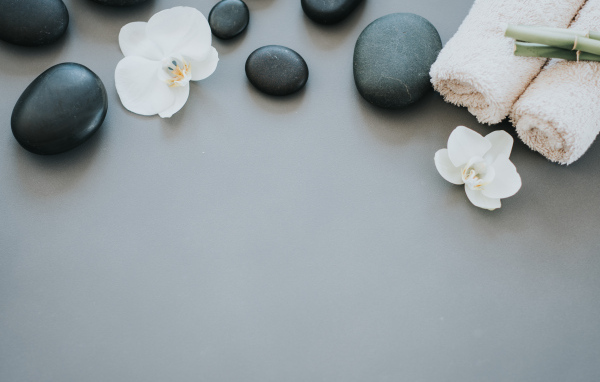 Черные камни с цветами орхидеи и полотенцем на сером фоне