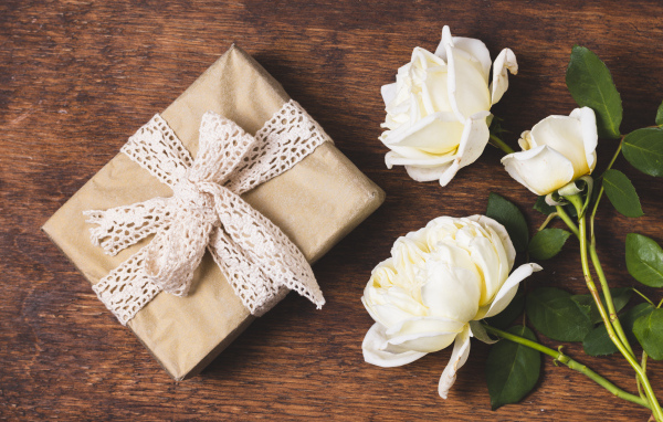 Коробка с подарком на деревянном столе с белыми розами
