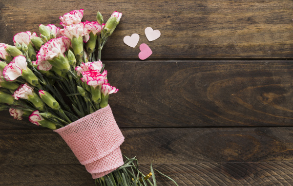 Розовые гвоздики с сердечками на коричневом деревянном фоне