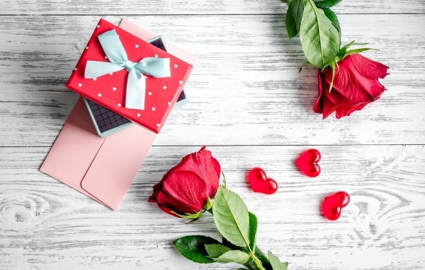 Две красные розы с подарком и сердечками на столе