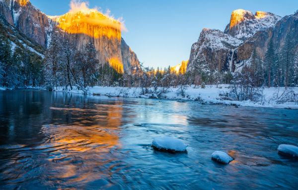 Холодная река с заснеженными берегами и горы в лучах солнца