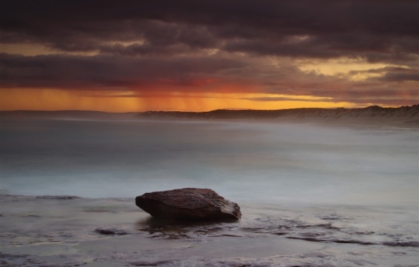 Большой камень в воде на фоне грозового неба в море