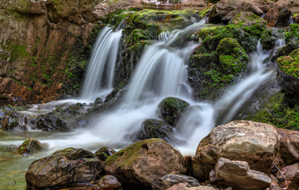 Быстрая вода водопада стекает по камням в осеннем лесу