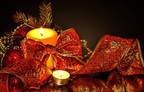 Зажженная свеча с красным бантом на черном фоне на Новый год