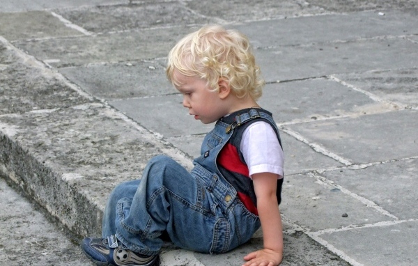 Мальчик в джинсовом комбинезоне сидит на дороге
