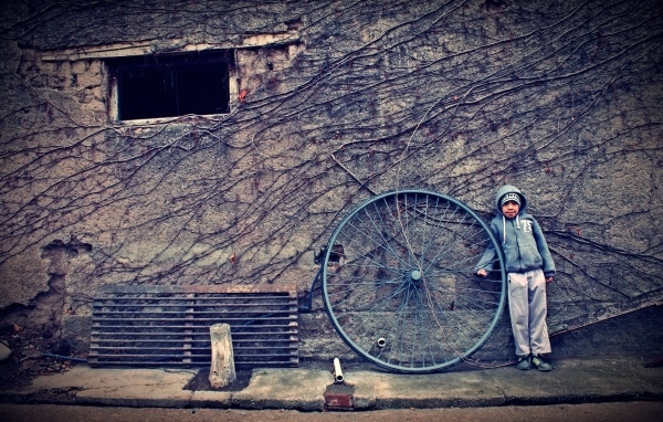 Мальчик с большим колесом стоит у стены