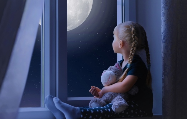 Маленькая девочка с игрушкой смотрит у окна на луну
