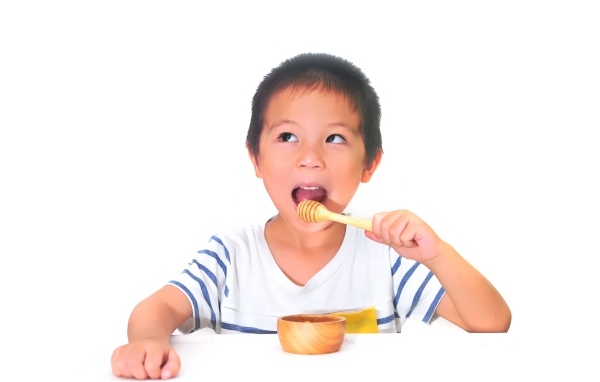 Мальчик азиат ест мед на сером фоне