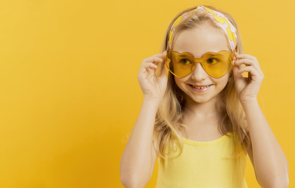 Красивая девочка блондинка в очках в форме сердца на желтом фоне