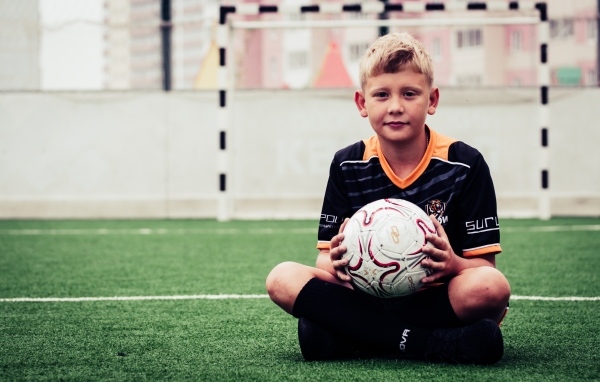 Мальчик футболист сидит на траве с мячом