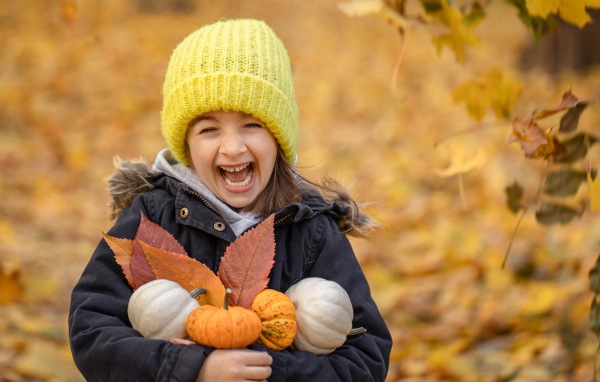 Cheerful girl with pumpkins and leaves in her hands in autumn