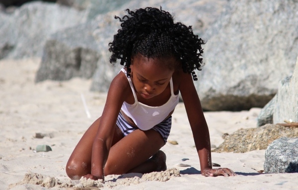 Темнокожая маленькая девочка играет на песке на пляже