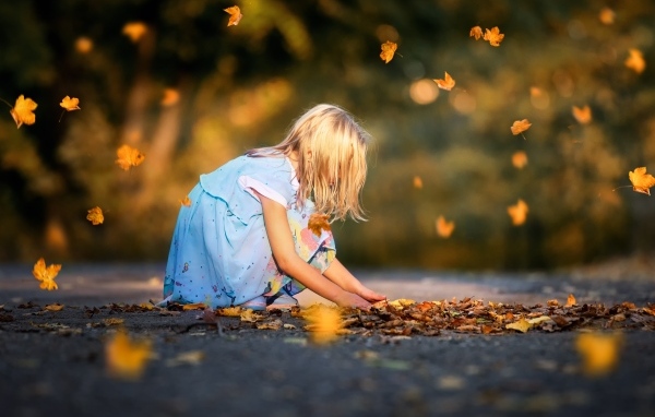 Девочка в платье играет с листьями на дороге