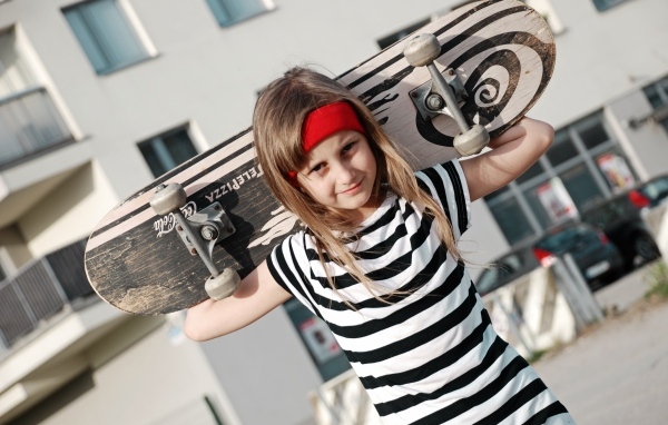 Девочка в полосатом платье со скейтбордом в руках