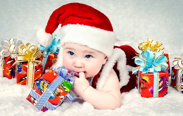 Грудной ребенок в новогодней шапке с подарками на покрывале