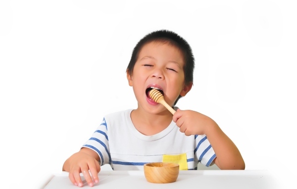 Маленький мальчик ест мед на белом фоне